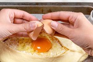 Female hands breaking a chicken egg into raw khachapuri