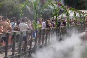 Festival visitors cool under flower gates with splashing water on Tomorrowland
