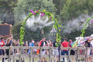 Festivalbesucher kühlen sich unter einem Blumentor mit Spritzwasser auf Tomorrowland
