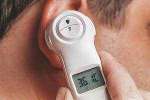 Fiebermessen bei einer Grippe und Erkältung: Mann benutzt ein schnelles Ohrthermometer / Fieberthermometer