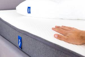 Flat hand lays on white and grey Casper mattress with memory foam, which relieves the body during sleep.