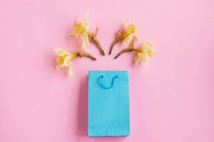 Flat lay of blue gift box and yellow spring flowers. Pink background.