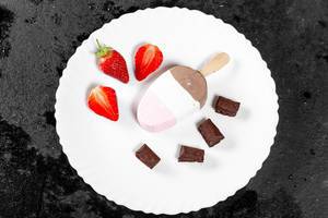 Flatlay von dreifarbigen Eis mit Schokoladenwürfeln und frischen Erdbeeren auf weißem Teller