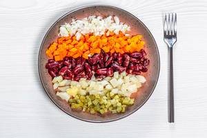 Flatlay von Gemüseplatte mit Zwiebeln, Karotten, Bohnen und Kartoffeln auf einem Holztisch