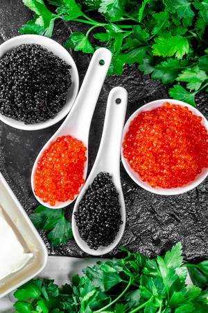 Flatlay von gesalzenem roten Lachskaviar und schwarzen Kaviar mit frischer Petersilie, auf einem Schiefersteinbrettchen