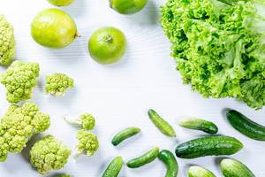 Flatlay von grünem Obst und Gemüse auf weißem Holztisch