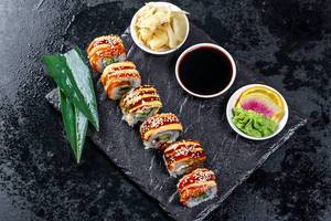 Flatlay von Rainbow Dragon Sushi Rollen mit Wasabi, Sojasoße und Ingwer auf schwarzem Tablett