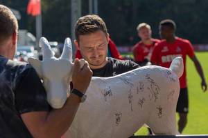 Florian Junge signiert eine Hennes VIII Figur mit Unterschriften der 1. FC Köln Spieler
