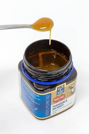 Flüssiger Honig tropft von einem Löffel ins Honigglas von Manuka Honey