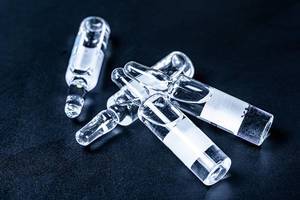 Flüssiges Arzneimittel in durchsichtigen Glasfläschchen auf dunklem Hintergrund Nahaufnahme