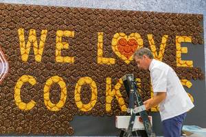 Food-Art auf der anuga Lebensmittelmesse: Mann kreiert ein Wandgemälde aus Keksen, mit dem Schriftzug "We love Cookies" (Wir lieben Kekse)