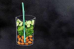 Food ingredients for blending smoothie -cucumbers, lettuce, almonds in painted glass on black chalkboard. Top view with copy space (Flip 2019)