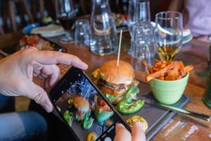 Food photography with the smartphone of a burger meal with sweet potato chips on a laid table in a Restaurant