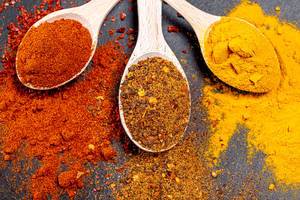 Fragrant spices. Ground paprika, turmeric and a mixture of peppers in wooden spoons