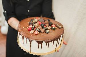 Frau hält einen großen Kuchen mit Schokoladenglasur, bunten Beeren und Schokoriegel-Verzierung
