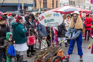 Frau im Kostüm mit Bauarbeiterhelm beim Rosenmontagszug, thematisiert Baumfällung für den Stadtbahnbau in der Bonner Straße