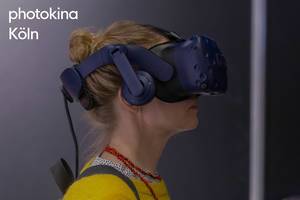Frau mit der blauen Virtual Reality Brille von HTC Vive im Seitenprofil, neben dem Bildtitel "photokina Köln"