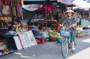 Frau mit Kegelhut auf einem Vintage-Fahrrad auf einem Marktplatz in Vietnam