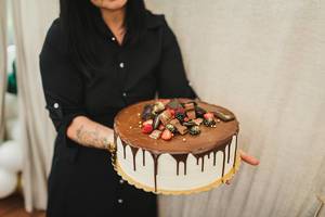 Frau trägt einen dekorativen Kuchen mit zerlaufener Schokolade und Beeren