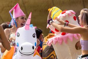 Frauen mit bunten Haare lachen und reiten auf aufblasbaren Einhörner auf dem Tomorrowland Festival