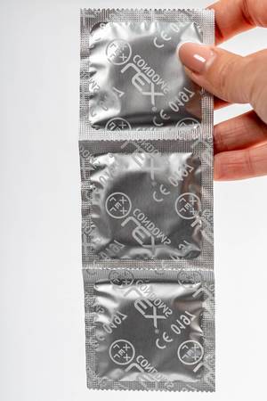 Frauenhand hält Kondomverpackungen vor weißem Hintergrund