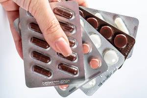 Frauenhand hält verschiedene Packungen von Medikamenten und Tabletten vor weißem Hintergrund