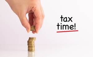 Frauenhand hebt Münzen auf mit dem Schriftzug "Tax Time"  (Zeit für die Steuern)