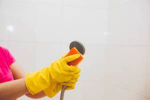 Frauenhände reinigen gründlich den Duschkopf mit einem gelben Schwamm