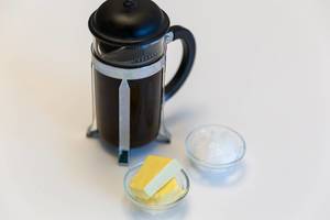 French Press Coffee maker, next to a glasbowl with butter and crushed ice