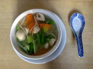 Fresh asian vegetable Soup in white bowl with a blue porcelain rice spoon on a wooden table
