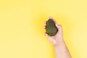 Fresh Avocado in the hand above yellow background