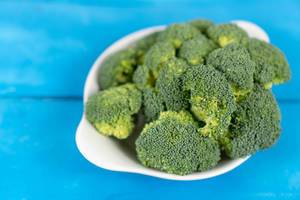 Fresh Broccoli in the bowl above blue wooden table