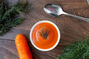 Fresh carrot and carrot puree soup with spoon on wooden background with dill (Flip 2019)