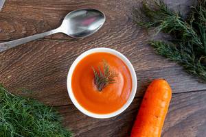 Fresh carrot and carrot puree soup with spoon on wooden background with dill