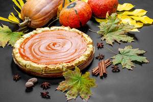 Fresh delicious homemade pumpkin pie with spices, pumpkins and autumn leaves on a black table (Flip 2019)
