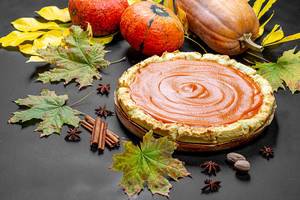 Fresh delicious homemade pumpkin pie with spices, pumpkins and autumn leaves on a black table