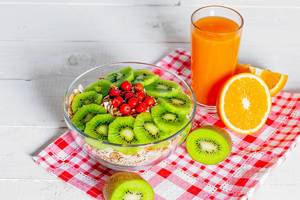 Fresh fruit orange and kiwi, a glass of juice and a plate of oatmeal on a checkered dish towel