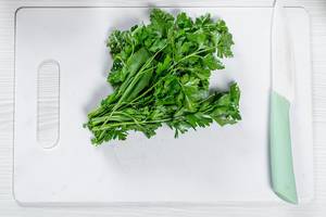 Fresh green parsley with a ceramic knife on a white kitchen Board