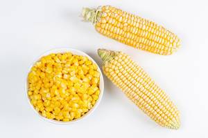 Fresh heads of corn and a bowl of boiled corn kernels, top view