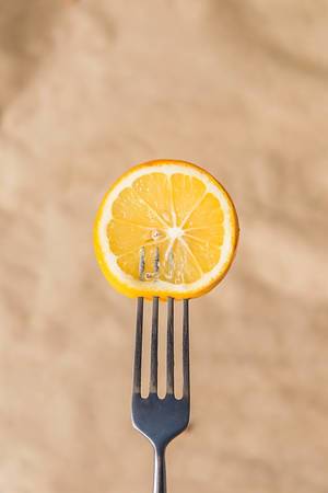 Fresh lemon slice on a fork against brown paper background (Flip 2019)