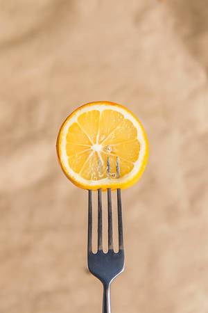 Fresh lemon slice on a fork against brown paper background