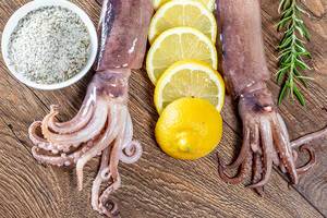 Fresh octopus or squids raw on wooden board with ingredients