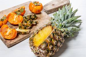 Fresh persimmon and pineapple fruit sliced on an old kitchen Board (Flip 2019)