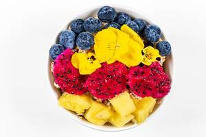 Fresh pieces of pitahaya, pineapple, blueberries and flowers with oatmeal on a white background, top view (Flip 2020)