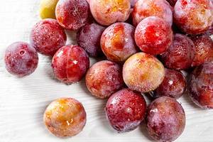 Fresh plums with water drops on white wooden background