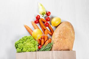 Fresh produce in paper grocery bag on white table