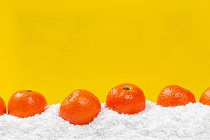 Fresh ripe tangerines on snow with yellow background behind with free space