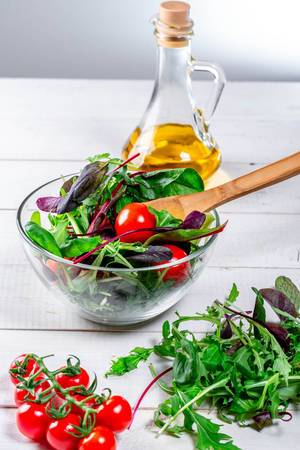 Fresh salad with arugula leaves, spinach, tomatoes and olive oil on a white wooden table