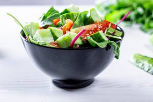 Fresh vegetable salad with arugula, spinach, tomatoes and cucumbers in a black mask
