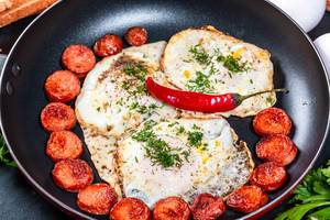 Fried chicken eggs and sausages in a frying pan